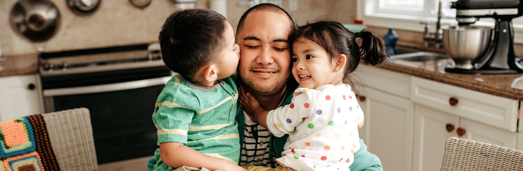 Loving father hugging his young son and daughter in their kitchen